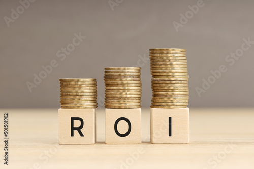 ROI word in wooden blocks with coins stacked in increasing stacks. Return on investment concept. Copy space