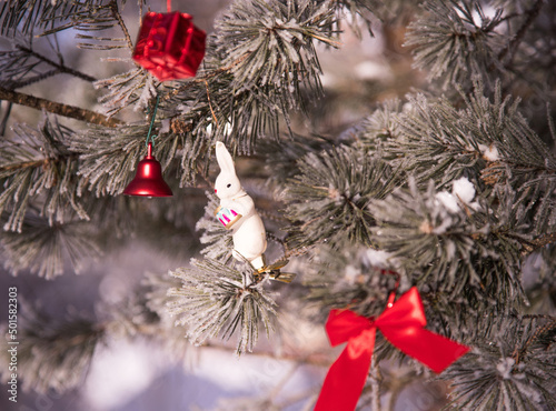 A snow-covered pine tree with red Christmas tree toys and a hare-the symbol of 2023. New Year's background