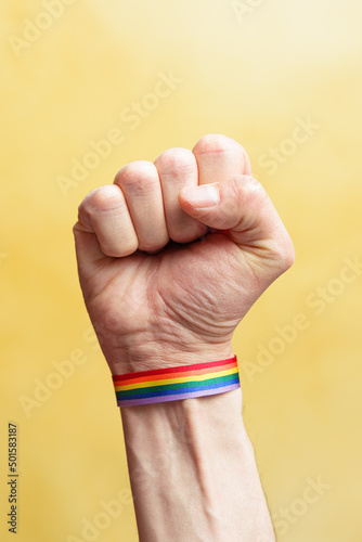 Fotografie, Obraz Raised fist with LGBT rainbow flag bracelet. Yellow background