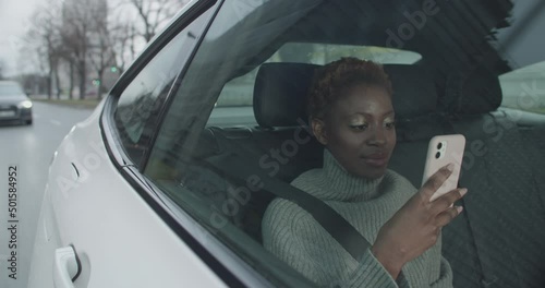 Young black woman car passenger is using her mobile phone while riding the uber