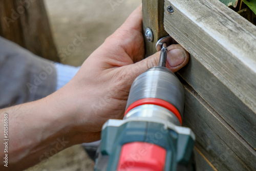 drilling tool in man's hands working close-up. Screwing bolts in wooden plank. Construction and building equipment and work 