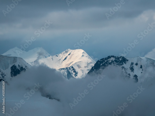 Wonderful minimalist landscape with big snowy mountain peaks above low clouds. Atmospheric minimalism with large snow mountain tops in cloudy sky.