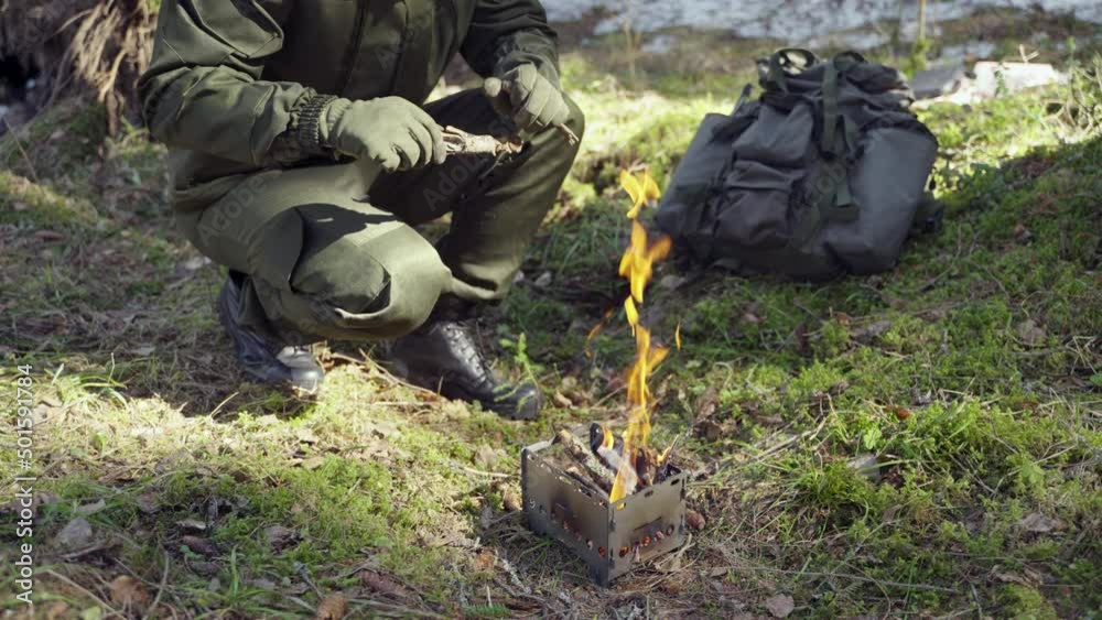 a man puts firewood in a portable folding stove against the backdrop of a forest. Bonfire in the camp. a man puts firewood in a portable folding stove against the backdrop of a forest. Bonfire in the camp.