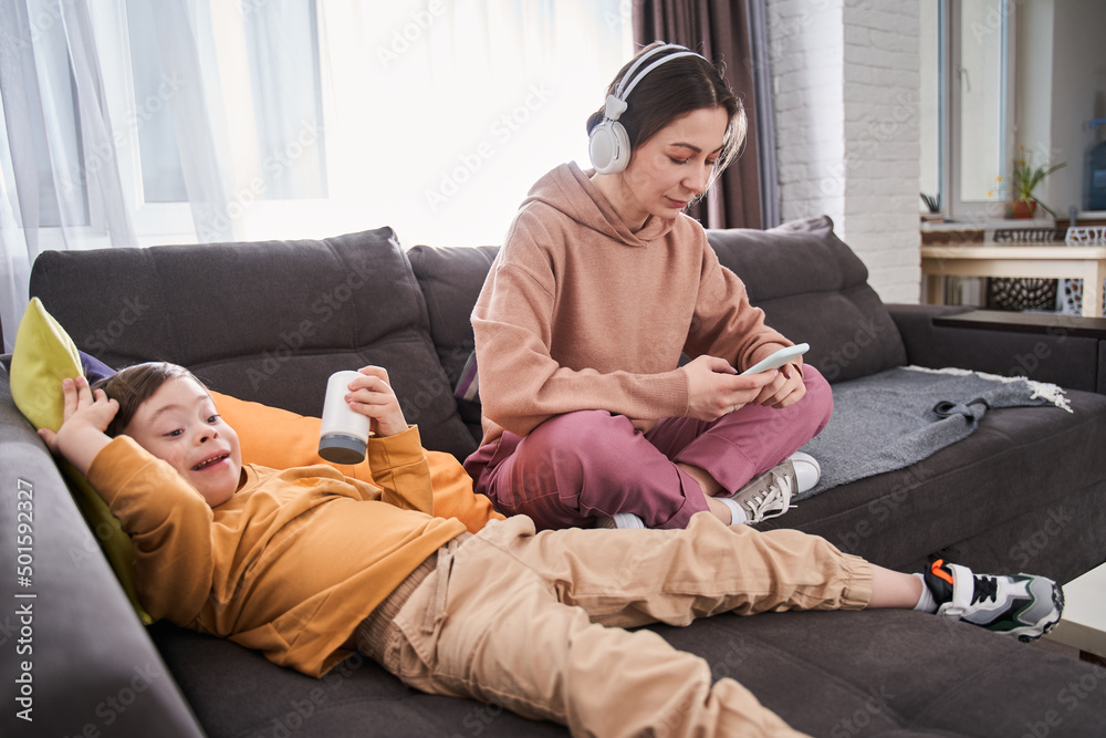 Obraz premium Boy with Down syndrome laying at the sofa with his mother and relaxing