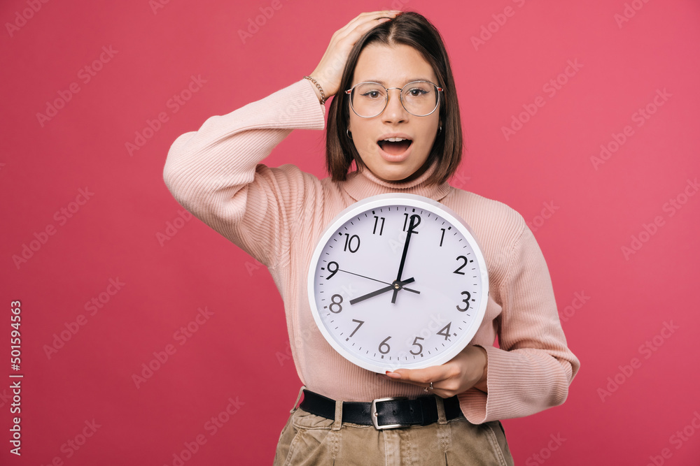 Surprised young woman is holding hand on head and a white round clock. Surprised young woman is holding hand on head and a white round clock.