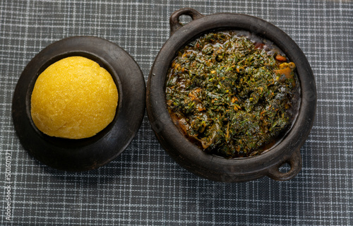Top shot of Efik Afang soup served in a clay bowl with garri on a textured background photo