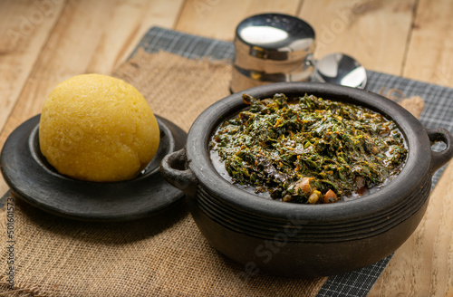 Efik Afang soup served in a clay bowl with garri on a wooden background photo