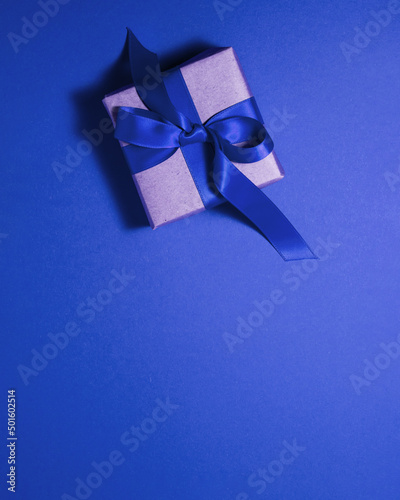 Brown paper gift box with a dark blue satin ribbon bow on blue background at the top with copy space. Flat lay father and mother day and presents concept