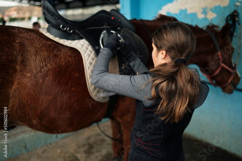 Girl with helmet and special clothes taking care of the horse after riding.