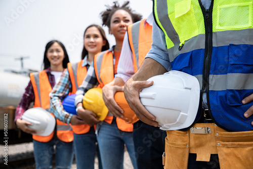 Teamwork of diversity engineer holding helmet standing in row on site work at train garage, banner cover digital design.