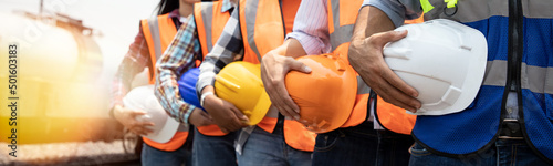 Teamwork of diversity engineer holding helmet standing in row on site work at train garage, banner cover digital design.