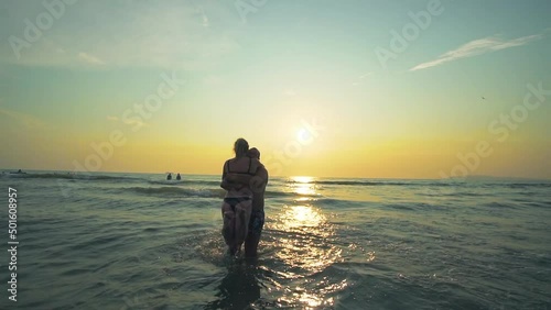 Couple in love having romantic tender moments, boyfriend lifting his girlfriend and turning arounf at sunset in the sea. Honeymoon and romantic vacation concept. Slow motion photo