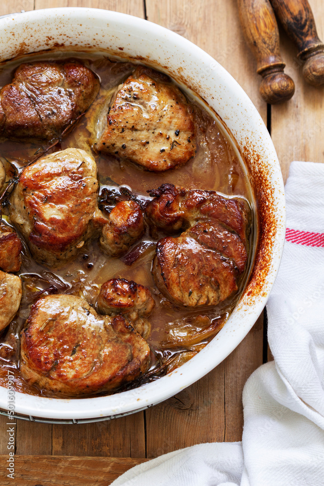 Tenderloin baked in onion sauce with herbs on a wooden table. Rustic style.