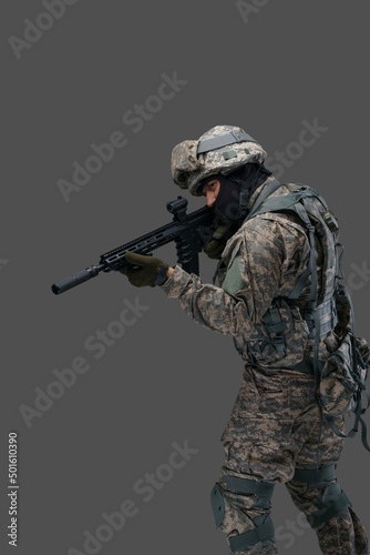 Phot of brave serviceman dressed in vest and uniform aiming rifle against gray background. © Fxquadro