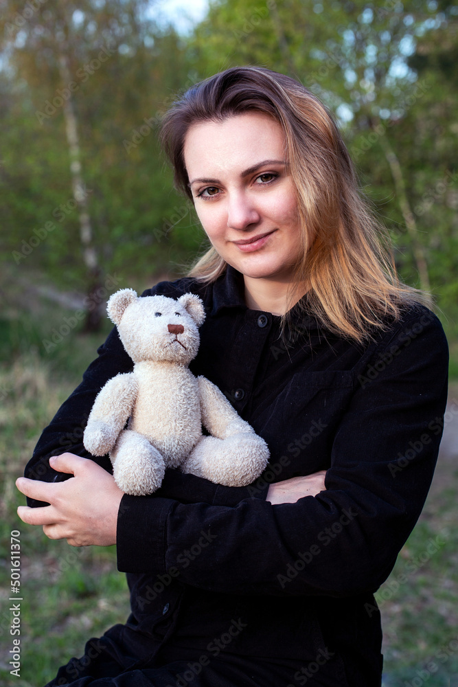 portrait of young woman holding a teddy bear outdoors in nature
