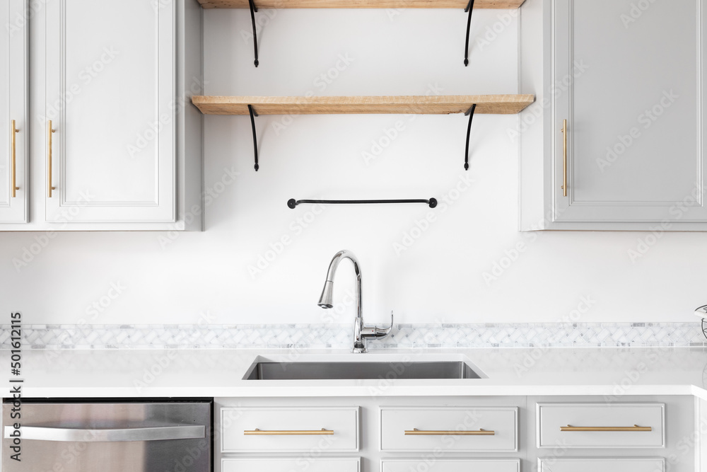 A modern farmhouse kitchen detail shot with grey cabinets, marble countertop and tiled backsplash, gold hardware, and wooden shelves. A modern farmhouse kitchen detail shot with grey cabinets, marble countertop and tiled backsplash, gold hardware, and wooden shelves.