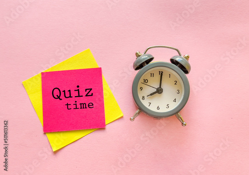 Sticky notes with quiz time message and alarm clock on a pink background 