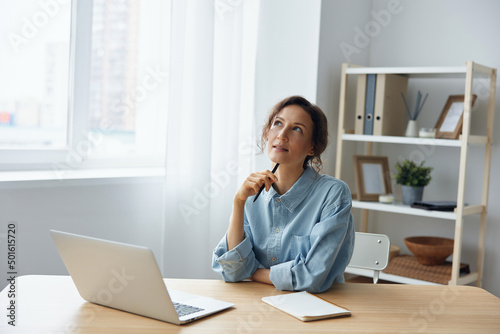 Dreaming thoughtful cheerful smart gorgeous pensive curly businesswoman think about weekend smiling looks aside using laptop in office. Modern Job Remote Work concept