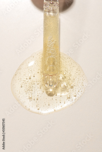 Top view of transparent pipette dropper with light golden drop of serum cosmetics, oil, gel ou cream on beige  background and bubbles of air. Minimal beauty concept, macro closeup with copy space photo