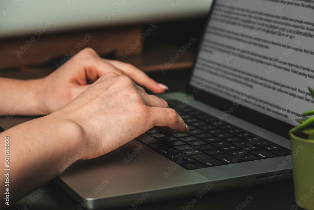 The girl is typing on a laptop text at the table. Photo of hands on the keyboard on the side The girl is typing on a laptop text at the table. Photo of hands on the keyboard on the side