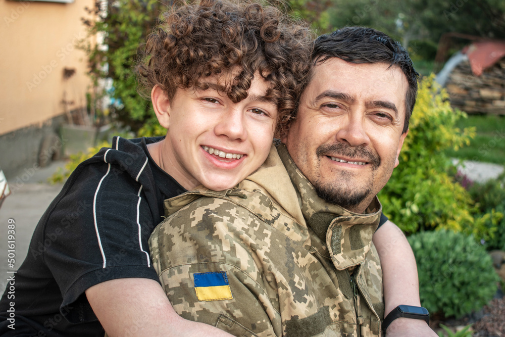 Teen son met with his father in the military of the Ukrainian army. Defender welcomes his family. Happy soldier. War in Ukraine. Military leave, rotation. Son hugs a dad Ukrainian soldier. Vacation