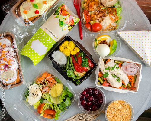 Ready food catering menu in lunch boxes as daily meal diet plan courier delivery with fork on white table background. Top view. Meat with vegetables, desserts, pie and a sandwich.