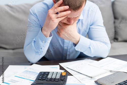 Distressed young man sit at desk paying bills feel stressed having financial problems. Unhappy upset male frustrated by debt or bankruptcy managing household budget or expenses photo
