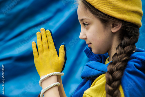 girl with a braid in a yellow sweater on a blue background with tied hands painted in blue and yellow Ukrainian flag