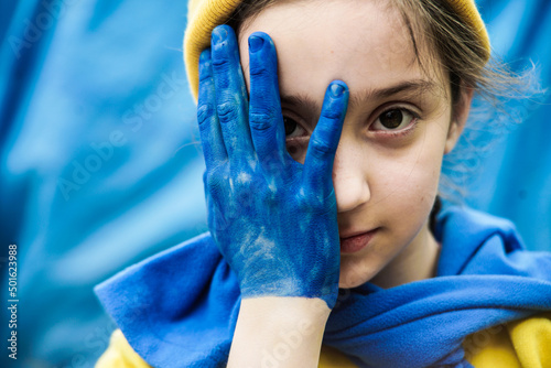 girl with a braid in a yellow sweater on a blue background with a hand painted in blue and yellow Ukrainian flag. Children ask for peace. Stop war