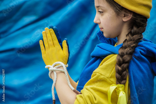 girl with a braid in a yellow sweater on a blue background with tied hands painted in blue and yellow Ukrainian flag
