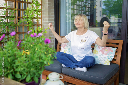 Senior woman relaxing in yoga pose on the cozy balcony at home. Active retirement, baby boomer generations. Terrace life in spring and summer. Sport and wellness in any age