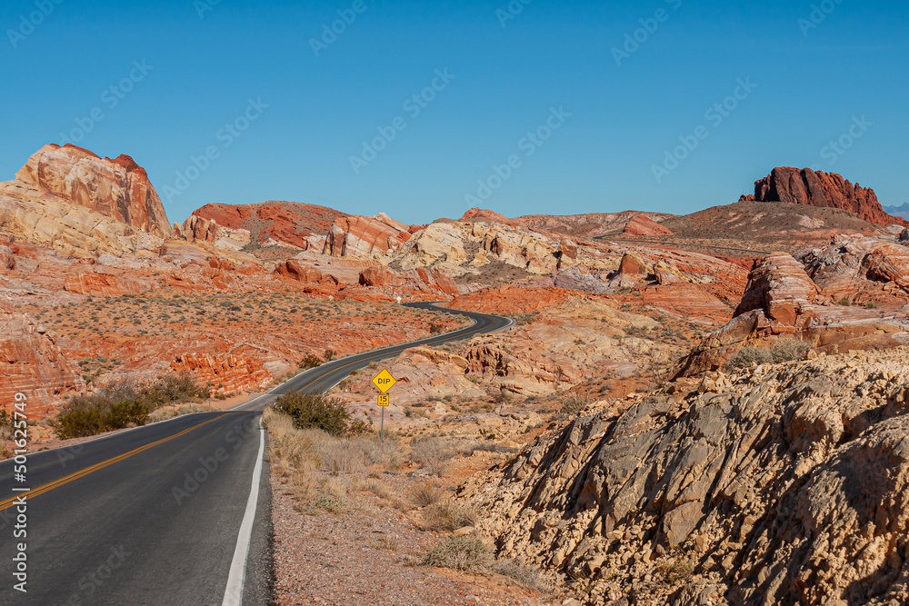 Overton, Nevada, USA - February 24, 2010: Valley of Fire. Wide desert landscape with black asphalt road with yellow divider dipping between red rocks while meandering under blue landscape,