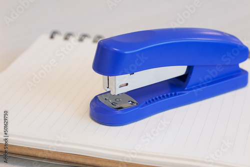 A blue stapler and a notebook on wooden office desk. Close up stapler photo