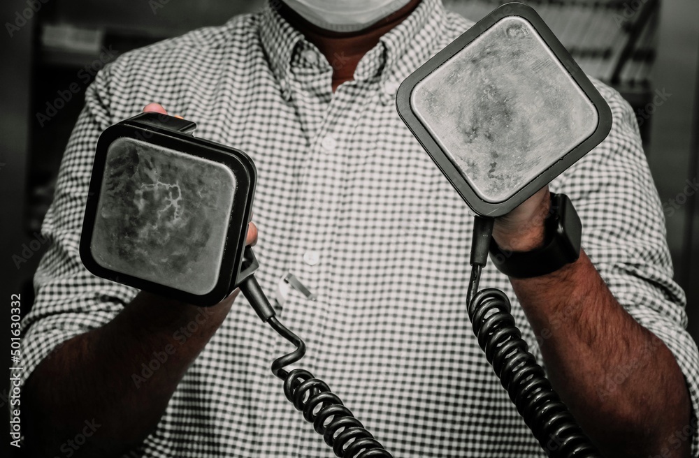 A health care worker holding paddles of a defibrillator . Defibrillator has two paddles to deliver shock called apex paddle and sternum paddle.. - obrazy, fototapety, plakaty 