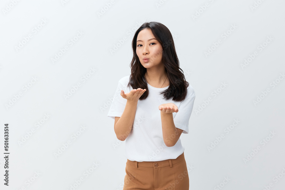 Cheerful lovely flirting cute Asian young female in white basic t-shirt sends kiss at camera posing isolated on over white studio background. The best offer for ad. People Lifestyle concept Cheerful lovely flirting cute Asian young female in white basic t-shirt sends kiss at camera posing isolated on over white studio background. The best offer for ad. People Lifestyle concept