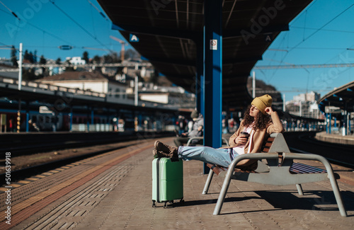Young traveler woman sitting alone at train station platform with luggage.