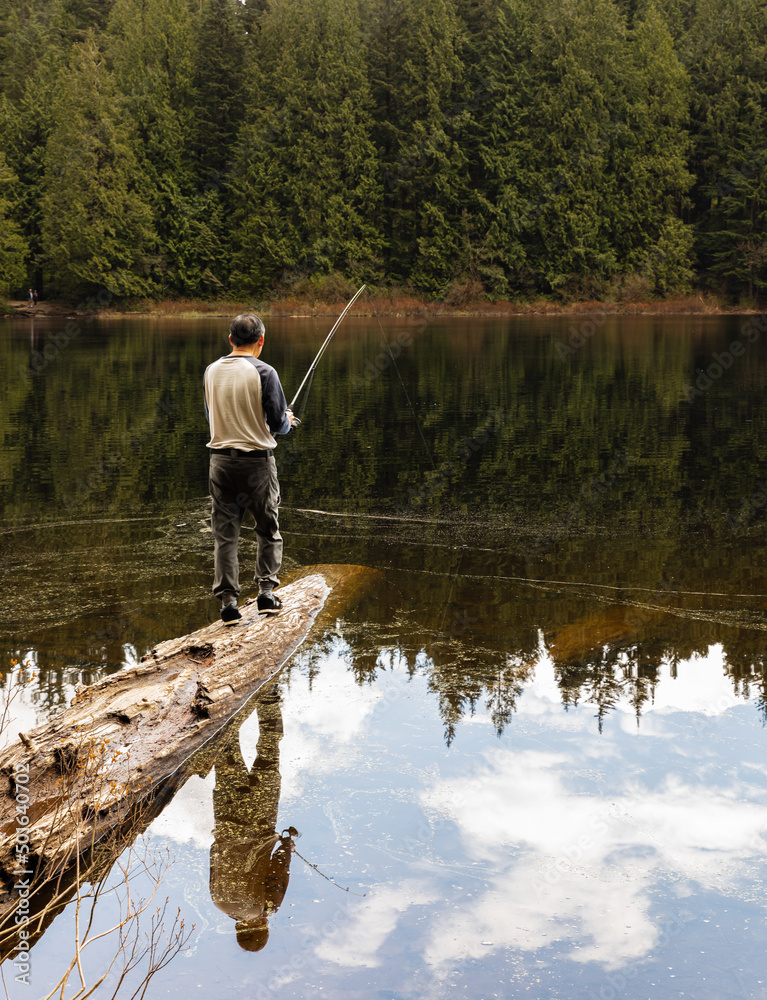 Man fishing alone at the lake in a forest. Fisher man fishing with fishing rod on a river bank at misty morning Man fishing alone at the lake in a forest. Fisher man fishing with fishing rod on a river bank at misty morning