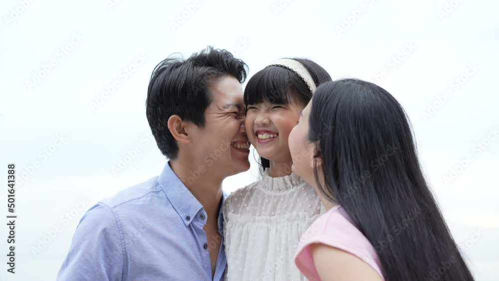 Holiday concept of 4k Resolution. Father and mother kissing daughter's cheek on the beach. Young Asian girl smiling happily. parents-child relationship. Holiday concept of 4k Resolution. Father and mother kissing daughter's cheek on the beach. Young Asian girl smiling happily. parents-child relationship.