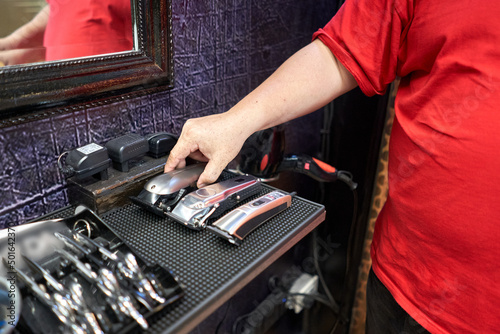 Barber taking a hair clipper from a table with several electric razors