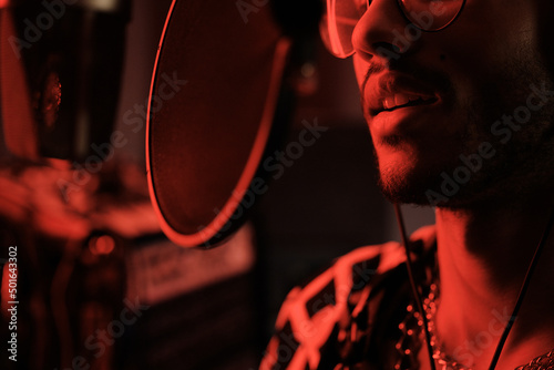 Close-up of handsome young Black professional singer recording song in modern studio in red neon light
