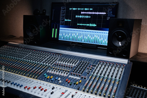 Horizontal no people shot of mixing console with sound settings and tracks on screen in modern recording studio