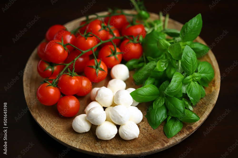 A set of products for caprese salad. Tomatoes, basil and mozzarella on a wooden board. A set of products for caprese salad. Tomatoes, basil and mozzarella on a wooden board.