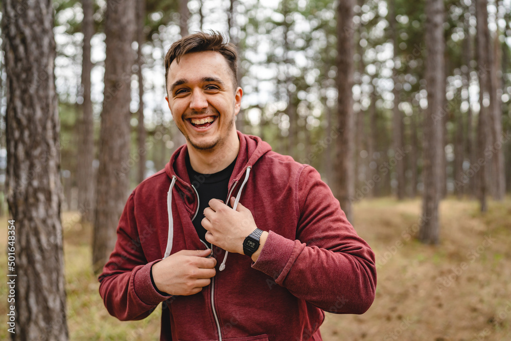 One man happy young caucasian male smiling while preparing to train in forest or public park putting on or taking off hoodie real people copy space One man happy young caucasian male smiling while preparing to train in forest or public park putting on or taking off hoodie real people copy space