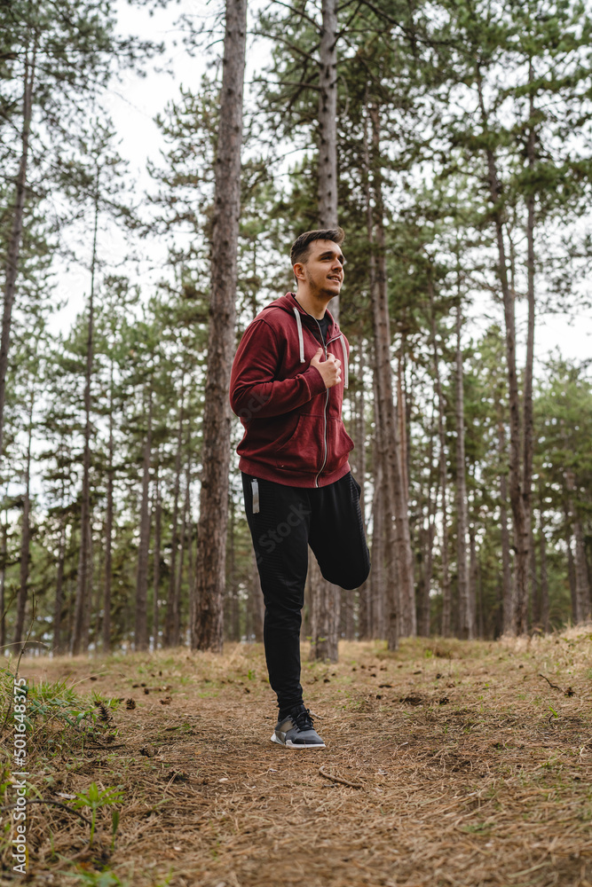 One man stretching in nature in forest or public park young adult caucasian male preparing for outdoor training in day standing alone real people copy space full length One man stretching in nature in forest or public park young adult caucasian male preparing for outdoor training in day standing alone real people copy space full length