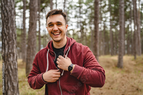 One man happy young caucasian male smiling while preparing to train in forest or public park putting on or taking off hoodie real people copy space © Miljan Živković
