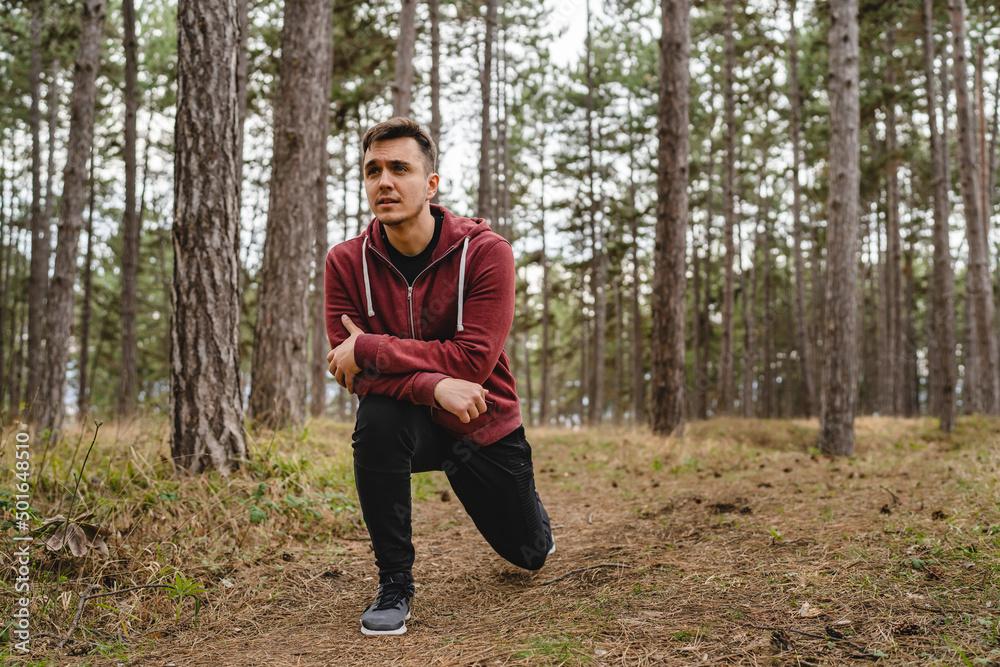 Obraz premium One man stretching in nature in forest or public park young adult caucasian male preparing for outdoor training in day standing alone real people copy space stretch leg full length