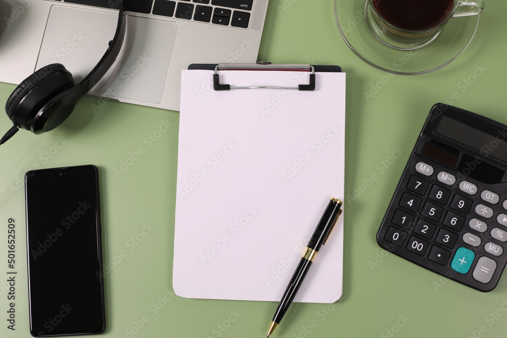 Modern green office desk with laptop computer, notebook, pen, eyeglasses, headphones, with coffee cup, calculator. Lay flat, top view, copy space