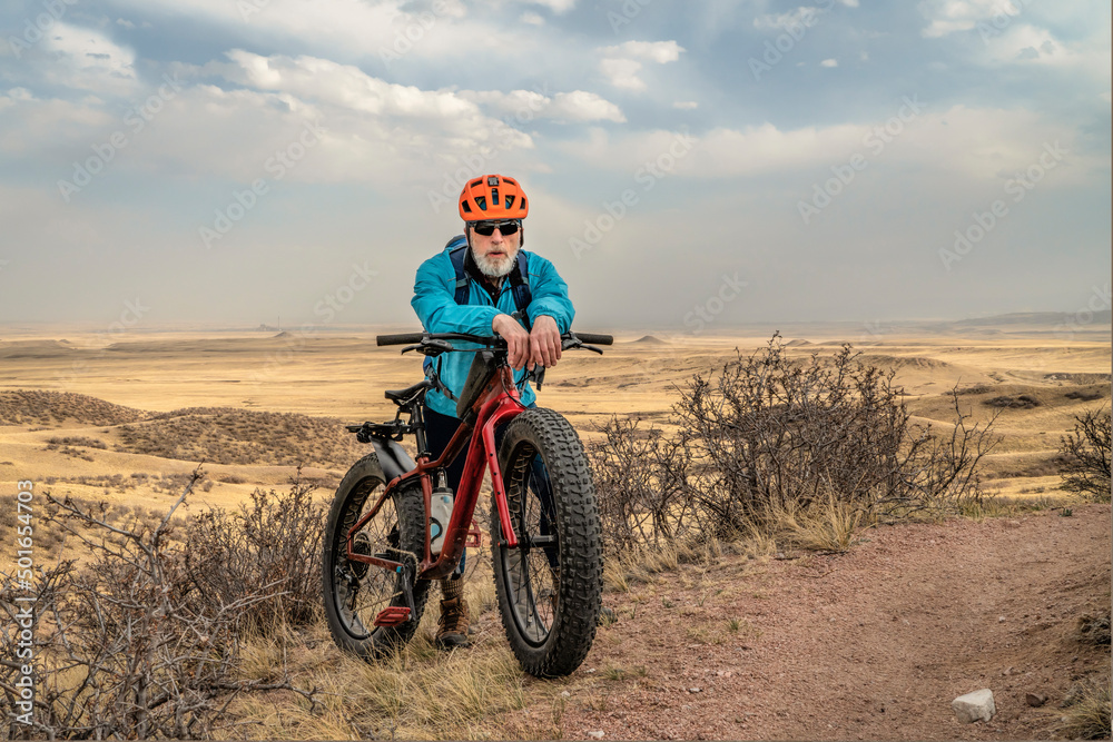 senior male cyclist with a fat mountain bike on a single track trail in northern Colorado grassland, early spring scenery in Soapstone Prairie Natural Area near Fort Collins