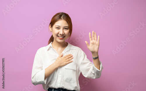 Optimistic, honest and cute asian girl give oath, swear tell truth, put hand on heart and raise one arm as making promise, express devotion and declare telling only truth, stand pink background. photo