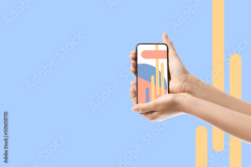 Female hands with modern smartphone on light blue background